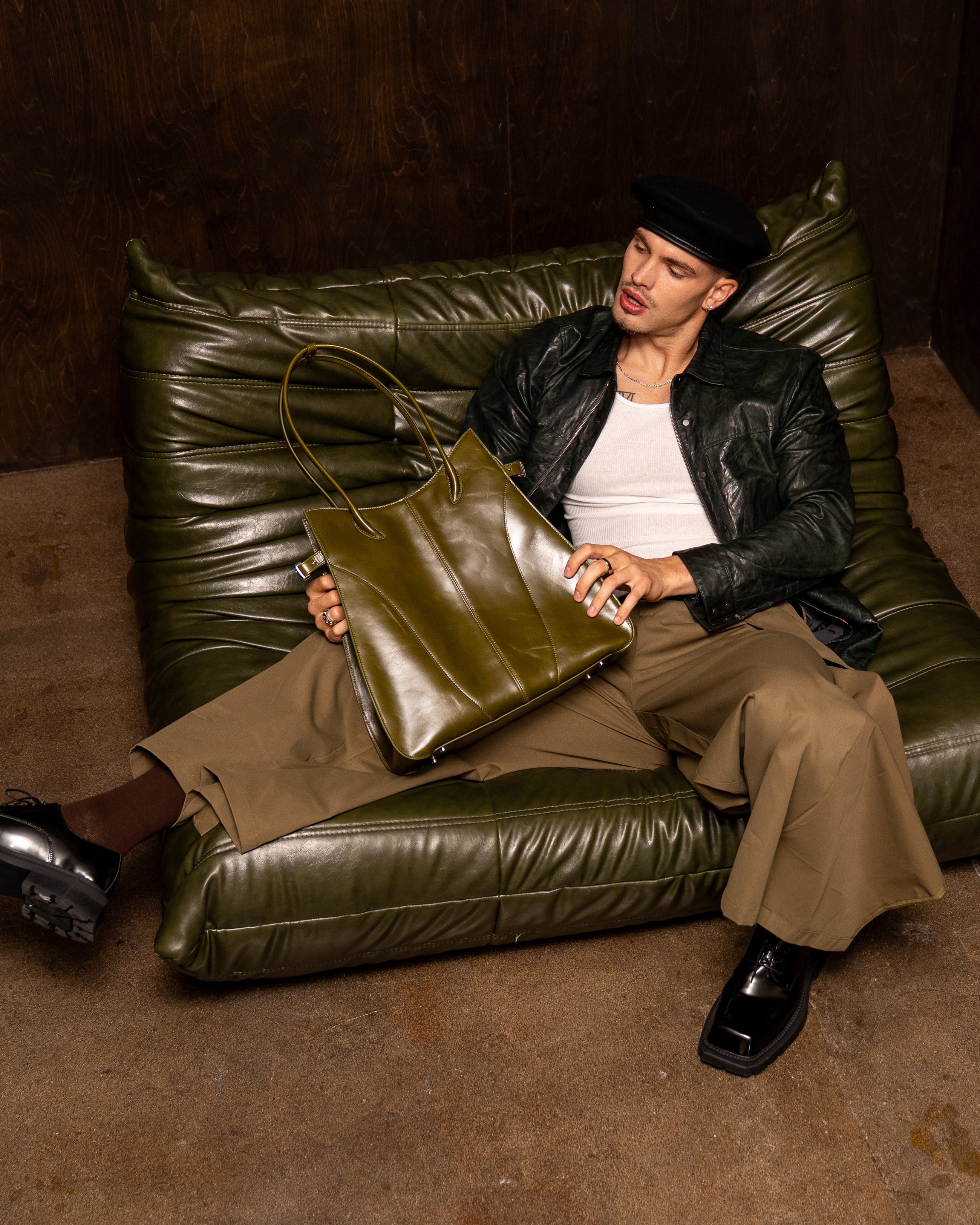 Person sitting on a green leather couch holding a green bag in a dimly lit room.