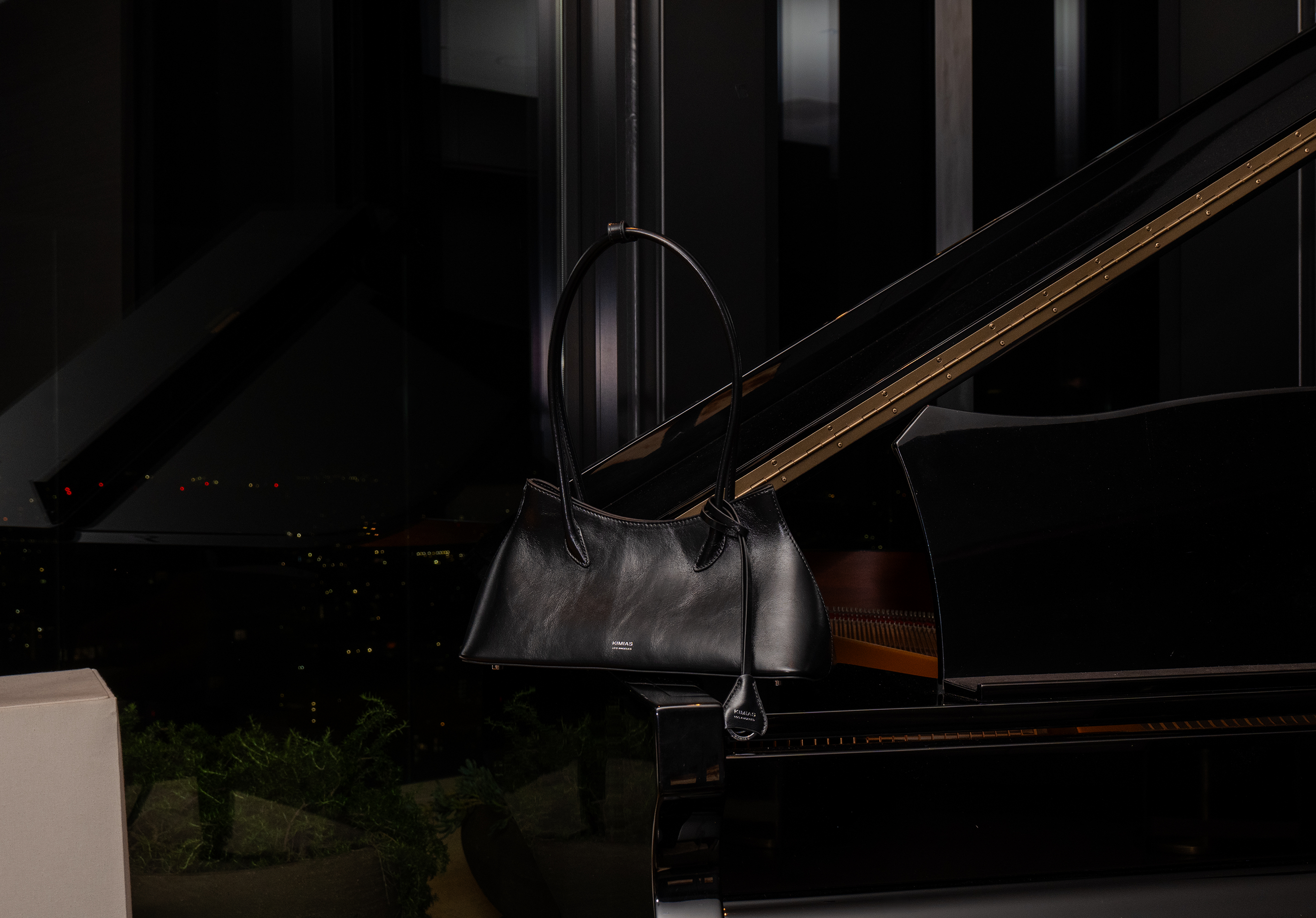Black KIMIAS handbag on a grand piano with a blurred cityscape background