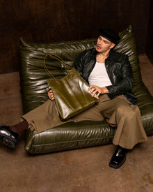 Person sitting on a green leather couch holding a green bag in a dimly lit room.