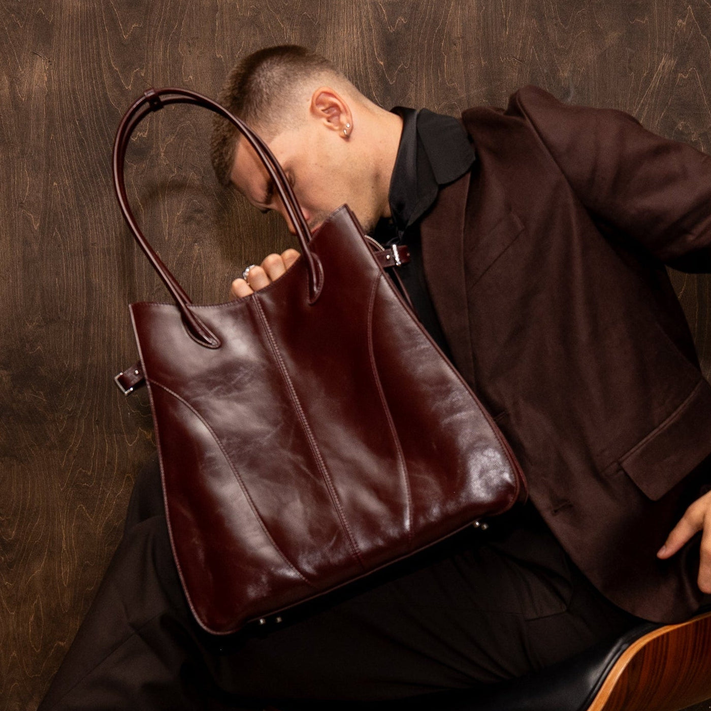 Man holding a leather bag in a dark room with a chair.