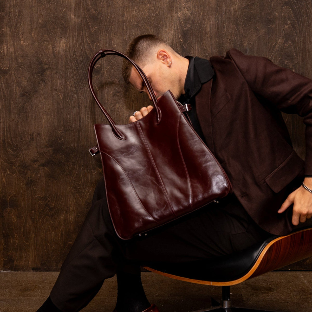 Man holding a large leather bag in a dimly lit room