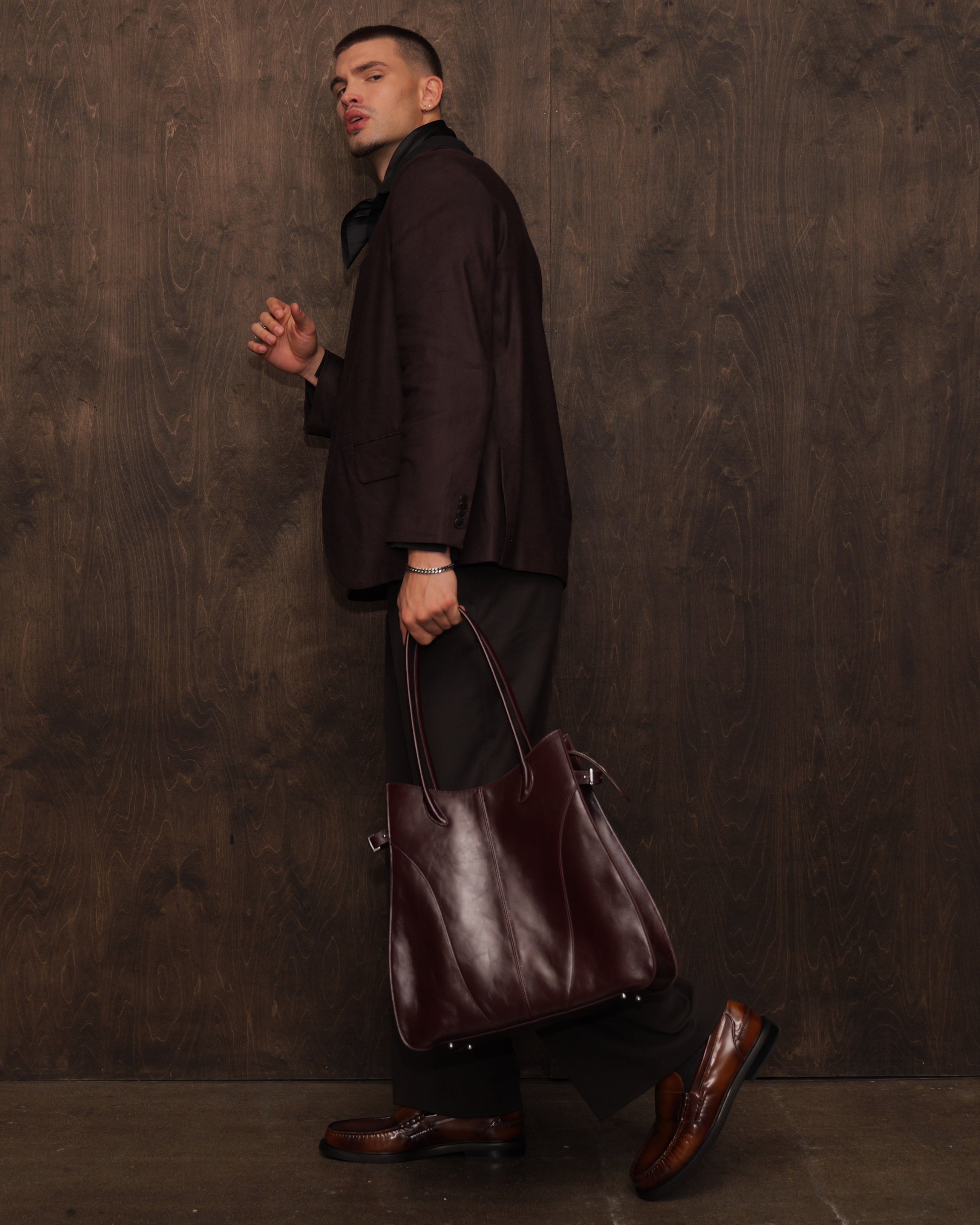 Man holding a leather bag against a textured brown wall