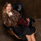 Woman sitting in a black chair holding a brown leather handbag against a dark background